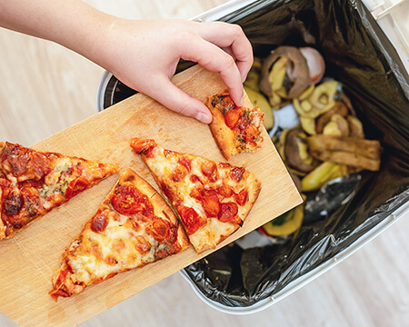 person putting pizza into school cafeteria trash