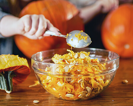 kids scooping out pumpkin seeds into a bowl