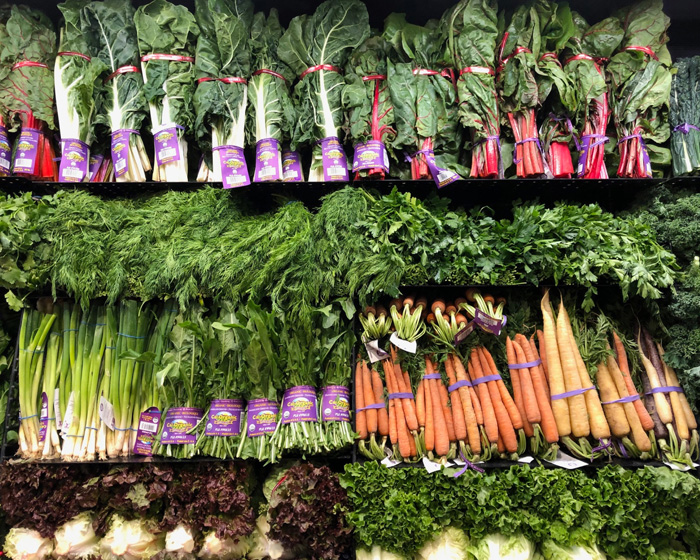 Grocery store produce section displaying leafy and root vegetables