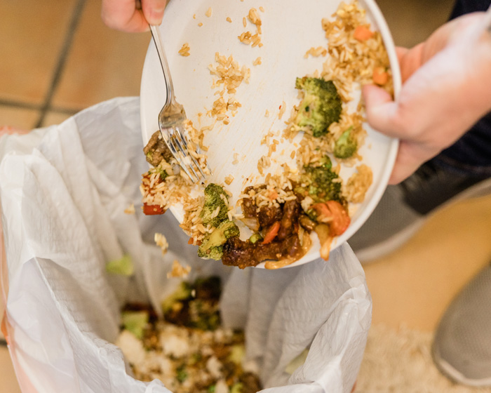 person throwing away foods into school cafeteria trash